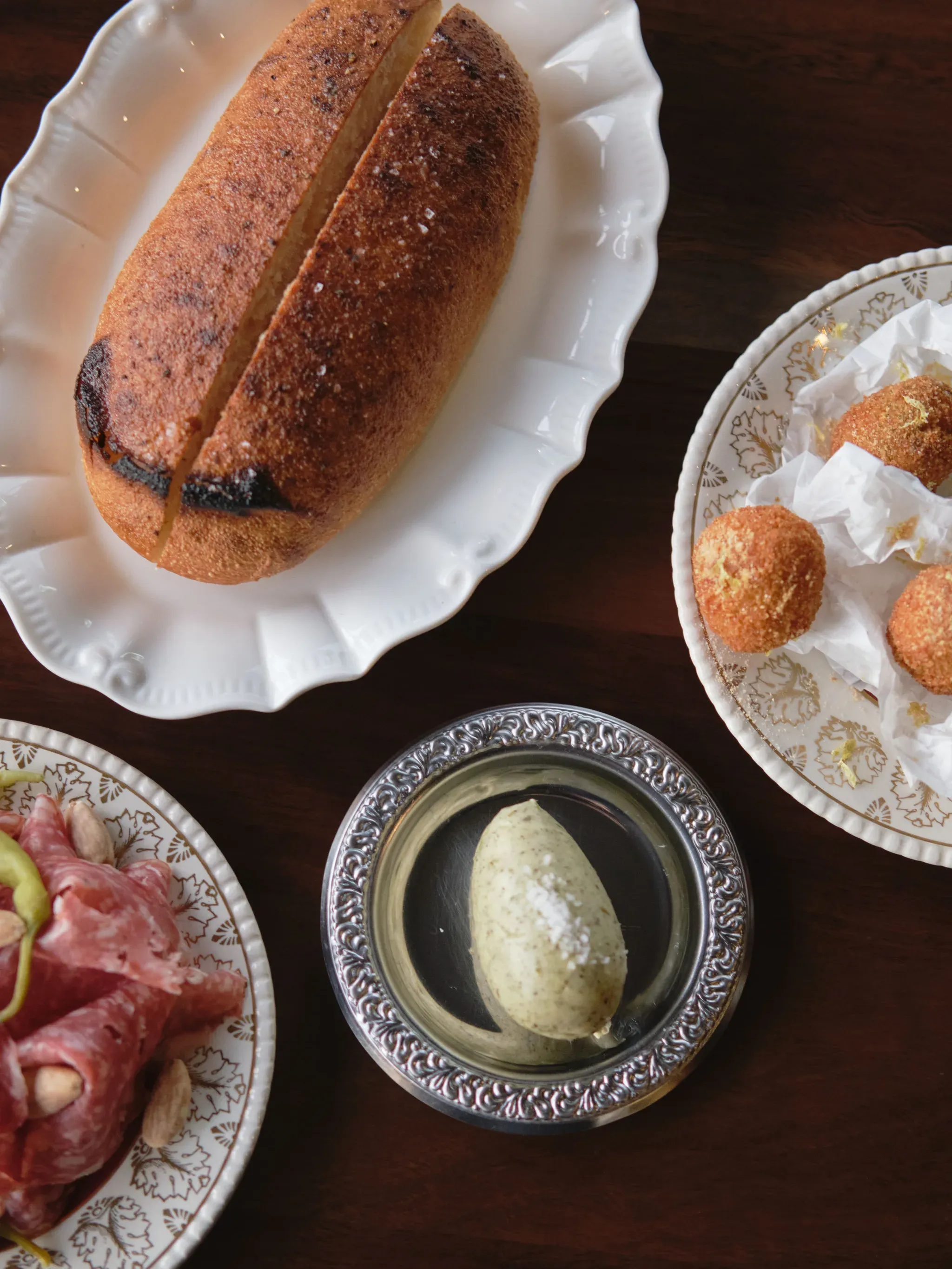 From above: a glazed loaf on a scalloped plate, fried croquettes, a dish of butter and sliced cured meat