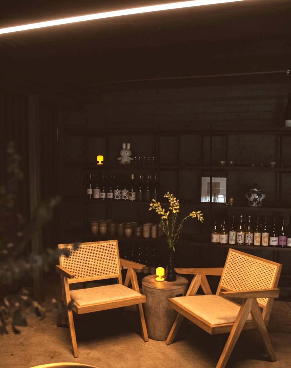 Two cane-backed timber armchairs around a small table with a candle and yellow flowers, shelves of bottles behind